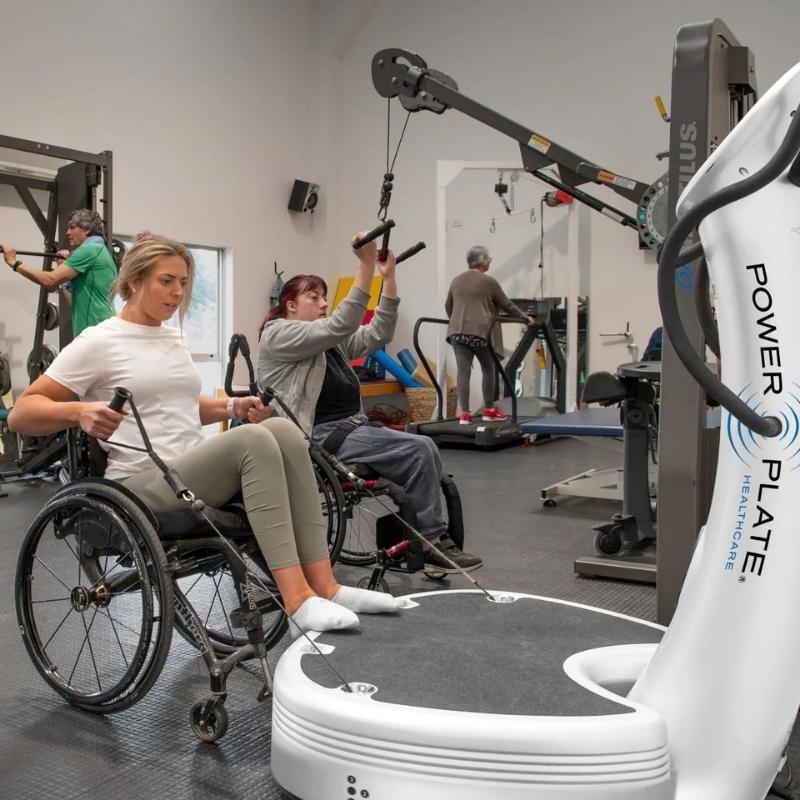 Two individuals using a Power Plate machine in a gym setting.