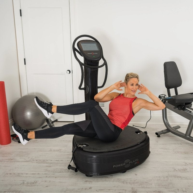 Woman exercising on a Power Plate machine in a home gym setting.
