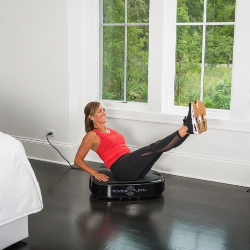 Woman exercising on a Power Plate machine in a room with large windows.
