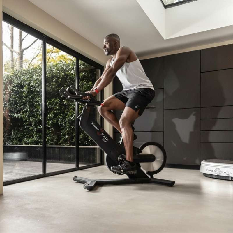 Man exercising on a stationary bike in a modern indoor setting with large windows.