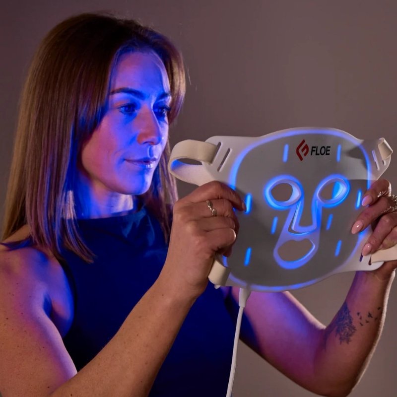 Woman holding a glowing face mask device with 'Floe' branding against a neutral background