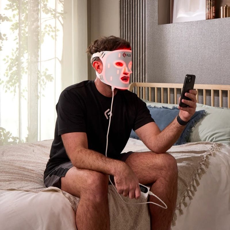 Person using a Floe red light therapy mask in a bedroom setting