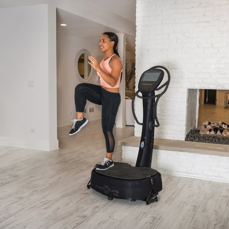 Woman exercising on a vibration plate machine in a home setting.