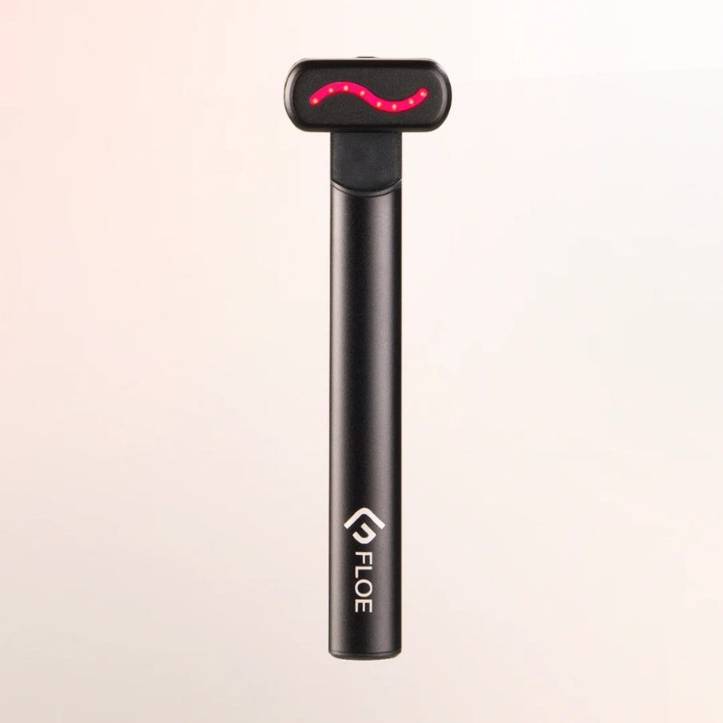 A black handheld Floe LED light therapy device with a glowing red light bar on the head, shown against a plain light beige background.